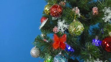 Bir Noel ağacı yanıp sönen bir bez ve çeşitli oyuncaklarla süslenmiş mavi bir arka planda dönüyor.