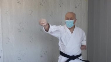 Tıbbi maske ve beyaz katategi ile yaşlı bir atlet elleriyle yumruk ve blok yapar.