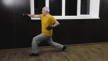 Kollarında siyah pedleri olan yaşlı bir sporcu atlamada iki yumruk sallıyor.