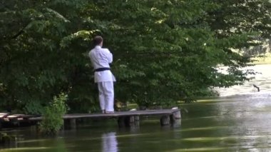 Bir atlet, gölün arka planında köprüde dikilirken resmi egzersizler yapıyor.