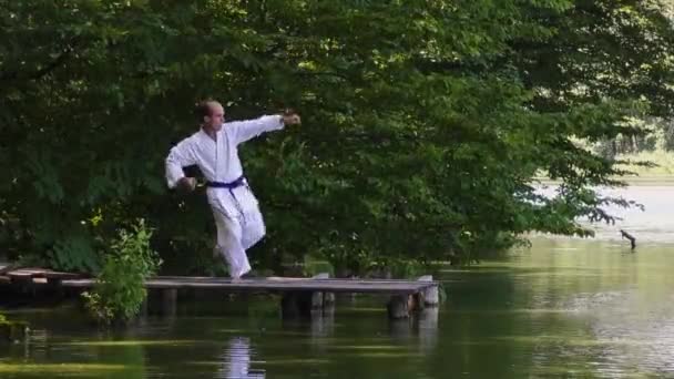 一名男子运动员在池塘的背景下打了几个拳 又踢上了桥 — 图库视频影像