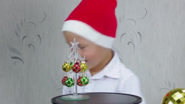 戴着圣诞老人帽的快乐的孩子正在看着圣诞树 — 图库视频影像