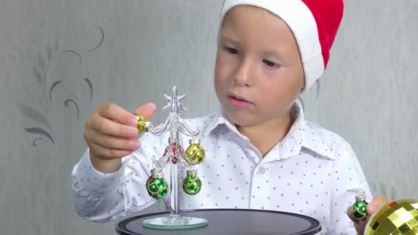Een Kind Een Kerstman Hoed Neemt Hangt Kerstversieringen Kerstboom — Stockvideo