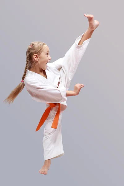 Girl on a gray background in karategi is a beating kick leg — Stock Photo, Image