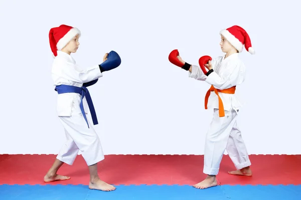 Sur les tapis rouges et bleus les sportifs en casquettes du Père Noël sont debout dans un rack de karaté — Photo