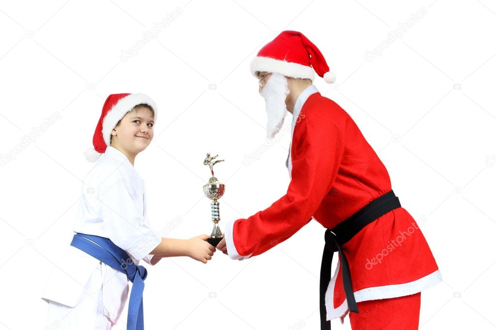 With black belt Santa Claus is giving the sportsman in karategi the cup karate