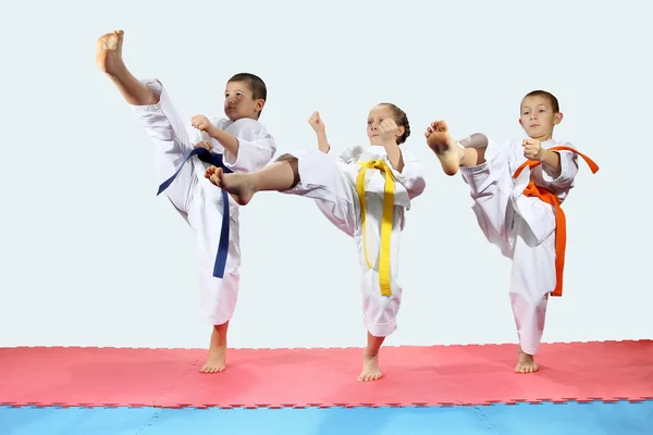Trois enfants en karategi frappent la jambe de pied vers l'avant — Photo