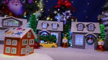 Kırmızı bir ev, dekore edilmiş bir Noel kasabasının arka planında, ışıklı bir tezgahta hareket ediyor.