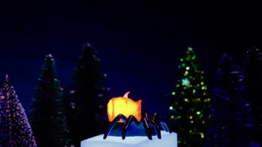 Örümcek şeklinde bir şamdanda sarı bir yapay mum Noel ağaçlarının arka planında dönüyor.