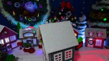 Büyük süslü bir Noel köyünün önünde dönen gri bir evin yakın çekimi.