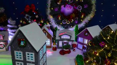 Arka planda köknar ağaçları ve büyük bir Noel çelengi olan büyük bir Noel köyünün önünde dönen gri bir evin yakın çekimi.