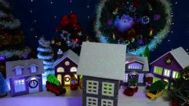 Noel ağaçları ve arka planında büyük bir Noel çelengi olan büyük bir Noel kasabasının önünde dönen dekore edilmiş bir evin yakın çekimi.