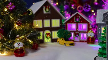 Noel ağaçlarıyla çevrili, büyük bir Noel köyünün merkezinde dönen gri bir evin yakın çekimi.