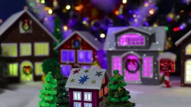 Noel ağaçlarıyla çevrili büyük, süslü bir Noel kasabasının merkezinde dönen küçük, koyu pembe bir evin yakın çekimi.