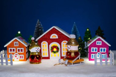 Üç renkli evin önünde kızaklarda kardan adamlar var ve onlar yok.