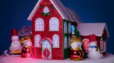 Mavi arka planda, bir Noel kasabası Noel evleri, kardan adamlar ve Noel ağaçları etrafında dönüyor.