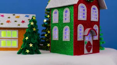 Mavi arka planda, pencerelerinde yanıp sönen ışıklar ve küçük Noel ağaçları olan dönen Noel evleri var.