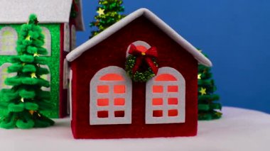 Mavi arka planda, küçük Noel ağaçları olan dönen Noel evleri var.