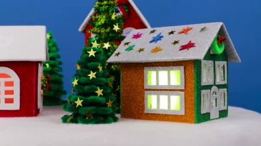 Mavi arka planda, pencerelerinde parlak ışıklar ve küçük Noel ağaçları olan dönen evlerin yakın çekimleri