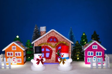 Küçük bir Noel köyünün ön tarafında siyah ve kırmızı şapkalı kardan adamlar var.