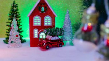 Ortadaki ışıkların arkasında Noel ağaçları ve arabalı bir ev var.