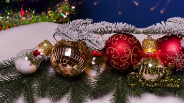 Ortasında ampuller olan büyük renkli toplar mavi arka planda beyaz ve yeşil Noel ağacının dallarına uzanır.