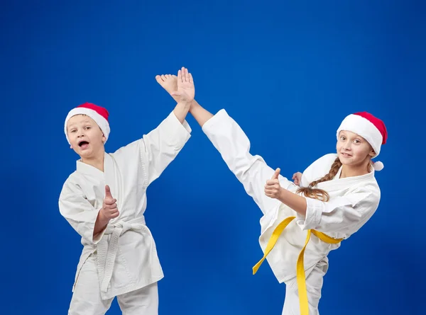 Dziewczyna i chłopak w czapki Santa Claus są szkolenia techniki karate i Wyświetlone jest Super — Zdjęcie stockowe