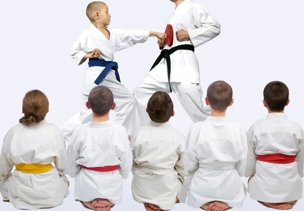 Vijf atleten zitten in pose kijken naar demonstratie punch karate — Stockfoto