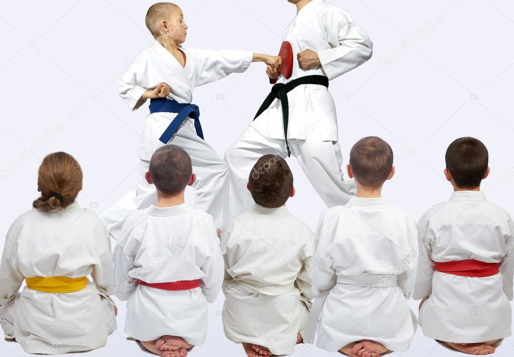 Five athletes sitting in pose looking at demonstration punch karate
