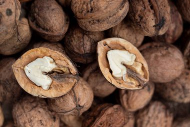 Çatlamış cevizlerin yakın çekimi beyaz fındık etini ortaya çıkarıyor. Arka planda sert kahverengi kabuklu cevizler var..