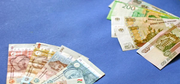 Photo of somoni bank notes from Tajikistan and Russian ruble bank notes on blue background.