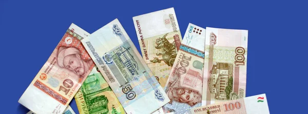 Photo of somoni bank notes from Tajikistan and Russian ruble bank notes on blue background. Banner size, copy space. Focus on money