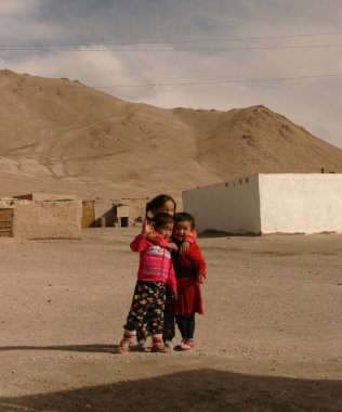 Murghab, Tacikistan, 10.2019: Pamir Otoyolu boyunca Murghab 'daki evlerinin önünde poz veren üç Tacikli çocuk