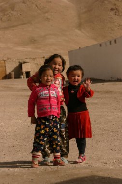 Murghab, Tacikistan, 10.2019: Pamir Otoyolu boyunca Murghab 'daki evlerinin önünde poz veren üç Tacikli çocuk