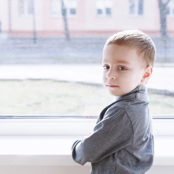 Liten pojke står nära fönster — Stockfoto