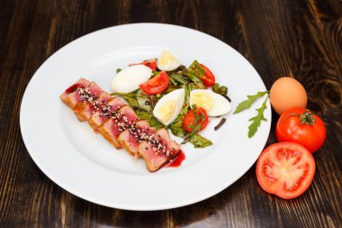 Beyaz tabakta susam sosuyla dilimlenmiş orta boy biftek. Haşlanmış kuşkonmaz, yumurta ve domatesle garnitür..