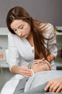 Genç ve güzel bir kadın yüz masajı yaptırıyor ve kremalı spa tedavisi görüyor.