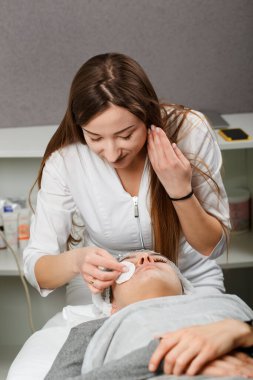 Genç ve güzel bir kadın yüz masajı yaptırıyor ve kremalı spa tedavisi görüyor.