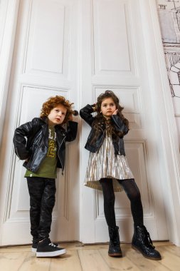 Deri ceketli kız ve erkek bir evin içinde birlikte poz veriyorlar.