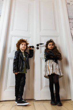 Deri ceketli kız ve erkek bir evin içinde birlikte poz veriyorlar.