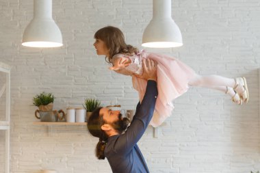 Mutlu genç adam, modern stüdyo salonunda küçük bir anaokulu kızını havaya kaldırıyor. Çok mutlu bir kız. Yakışıklı babasıyla eğleniyor. Evde uçuyor..