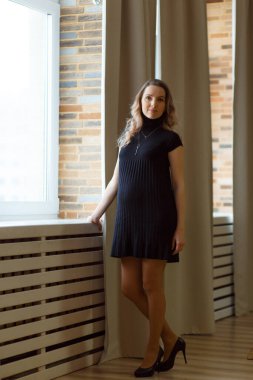 Düşünceli hamile kadın karnını okşuyor ve kameraya bakıyor. Tam uzunluk.