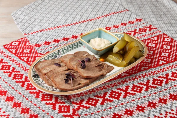 ベラルーシの装飾が施されたテーブルクロスで提供される楕円形のプレート上に馬肉と漬物とスパイシーな煮込み牛肉の舌 — ストック写真