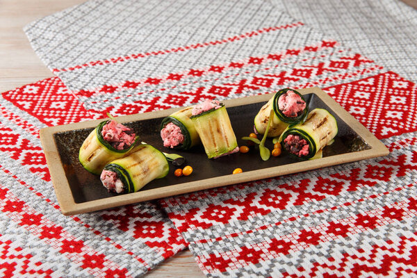 Grilled Zucchini rolls with homemade cheese and dried beetroot served on napkin with national belorussian ornament