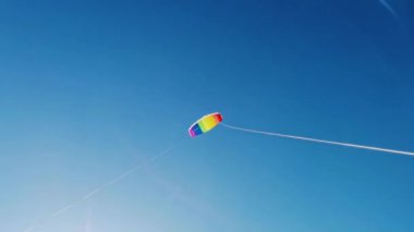 Yazın güneşli bir günde, gün batımında arka planda mavi gökyüzüne uçan gökkuşağı renkli uçurtma. Çocukluğunda iki el rayı ile uçurtmaya rehberlik etmiş. Özgürlük için. Oyuncak. 4k.