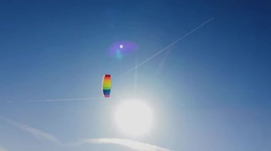 Yazın güneşli bir günde, gün batımında arka planda mavi gökyüzüne uçan gökkuşağı renkli uçurtma. Çocukluğunda iki el rayı ile uçurtmaya rehberlik etmiş. Özgürlük için. Oyuncak. 4k.