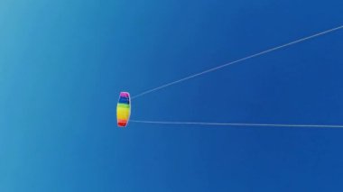 Yazın güneşli bir günde, gün batımında arka planda mavi gökyüzüne uçan gökkuşağı renkli uçurtma. Çocukluğunda iki el rayı ile uçurtmaya rehberlik etmiş. Özgürlük için. Oyuncak. 4k.