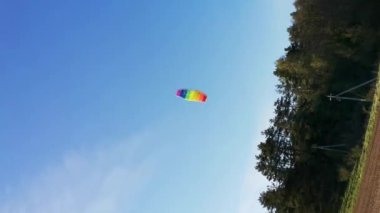 Mutlu çocuğun dikey videosu tarlada rüzgarla oynayarak gökyüzüne parlak bir gökkuşağı uçurtması fırlatıyor. Yaz konsepti. Okul tatili. Yaşam tarzı. Çocukluk