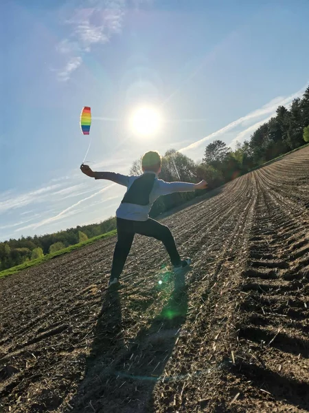 Un ragazzo felice lancia un aquilone arcobaleno luminoso nel cielo in un campo arato — Foto Stock