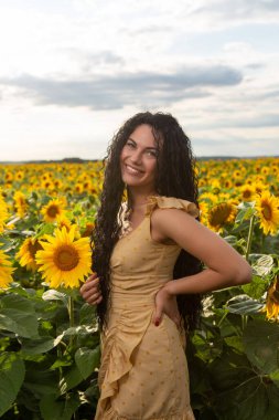 Güzel, gülümseyen, koyu saçlı, elinde bir buket ayçiçeği olan bir kadının portresi.